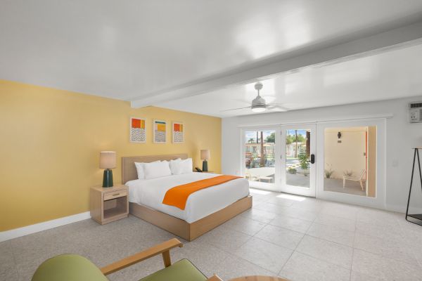 A modern bedroom with a large bed, orange accents, nightstands, a ceiling fan, and large glass doors opening to an outdoor area it features.