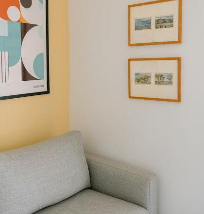 A light gray sofa is placed against a two-tone wall with abstract and framed artwork above, featuring geometric shapes and images in wooden frames.