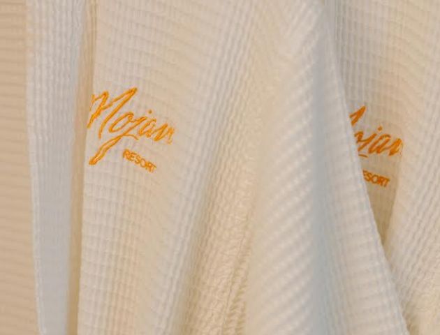 The image shows two white waffle-weave bathrobes hanging side by side with the word 