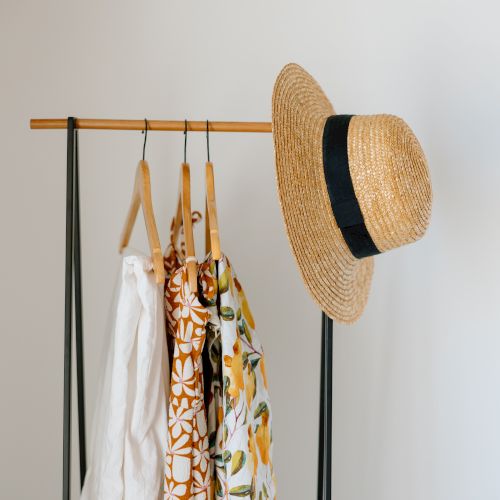 The image depicts a clothing rack with several patterned garments on hangers and a straw hat with a black band hung on one side.